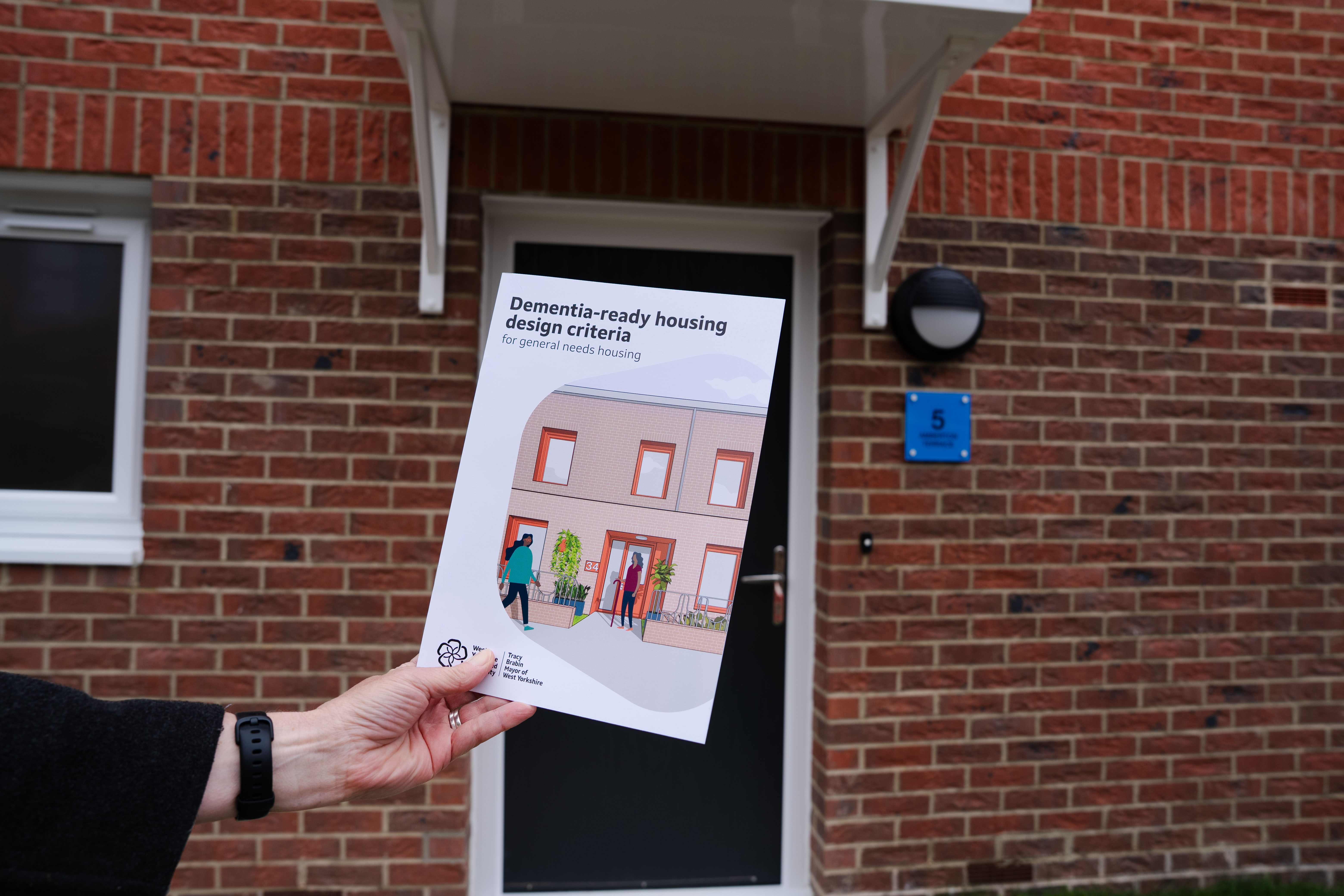 Dementia-ready housing design criteria document held up with front door of home in background